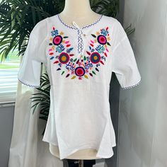 a white top with colorful flowers on it sitting next to a potted palm tree