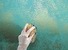 a person in white gloves holding up a hamburger on top of a blue surface with green paint