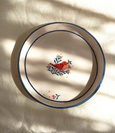 a plate with a red bird painted on it sitting on a white cloth covered table