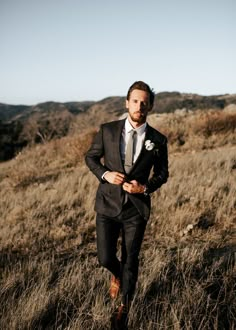 a man in a suit and tie walking through tall grass