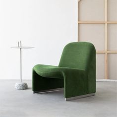 a green chair sitting on top of a cement floor next to a table and lamp