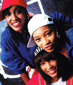 three young women are posing for a photo in front of a graffiti covered wall and one is wearing a baseball cap