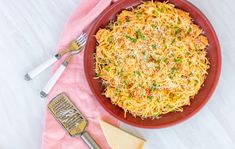 a red bowl filled with pasta and cheese on top of a pink napkin next to silverware