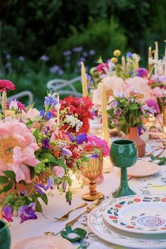 the table is set with colorful flowers, candles and china plates for dinner guests to enjoy