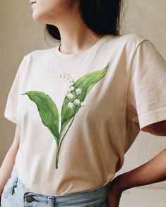 Celebrate May Birth Flower with our Lily of the Valley t-shirt. This original watercolor print that you will not find anywhere else will make a perfect gift for someone who celebrates a birthday in May. Printed on a cotton t-shirt, made from durable lightweight cotton. Unisex fit - boxy and long. How it's made: * All prints are original watercolor designs hand-painted by a botanical artist. * Ethically made 100% cotton t-shirts that are made to last. * T-shirts are printed and shipped by my prin Plants Print Crew Neck T-shirt Gift, Plants Print Crew Neck T-shirt For Gift, Crew Neck T-shirt With Plants Print, Hand Painted White T-shirt For Summer, Spring Gift White T-shirt, Spring Gift T-shirt With Graphic Print, Spring Graphic Print T-shirt Gift, Floral Print Graphic Tee T-shirt As Gift, Floral Print T-shirt For Spring Gift