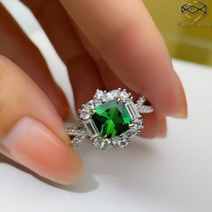 a woman's hand holding a ring with a green stone in the center and white diamonds around it