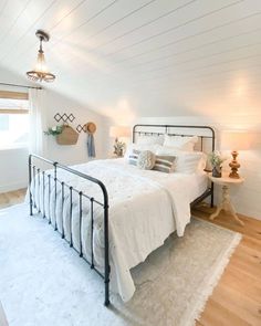 a bedroom with white walls and wood flooring has a metal bed frame in the middle