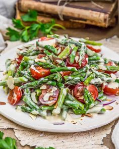 a white plate topped with asparagus and tomato salad next to a stack of books