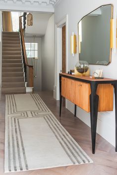 a living room with a rug, table and mirror on the wall next to stairs