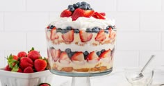 a dessert with strawberries, blueberries and cream in it on a white table