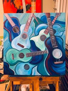 an artist's easel with two guitars painted on it and another painting in the background