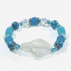 This 7" stretch bracelet has gorgeous shades of blue, teal, and turquoise with a shimmering glass shell focal point bead. Please treat your jewelry with care and it will last for many years. Do not submerge or wear your jewelry in water, pools, sauna's, steam rooms, etc. Metal components are nickel and lead free. Please note that the actual color may vary slightly, as device screens may differ. CHOKING HAZARD! Small parts included.  Not intended for children age 3 and under. Blue Spiritual Stretch Bracelet For Beach, Spiritual Blue Stretch Bracelet For Beach, Handmade Turquoise Crystal Bracelet For Beach, Handmade Turquoise Beaded Bracelets In Ocean Style, Turquoise Bohemian Crystal Bracelet For Beach, Bohemian Turquoise Crystal Bracelet For Beach, Spiritual Turquoise Stretch Bracelet For Beach, Handmade Adjustable Turquoise Stretch Bracelet, Handmade Turquoise Stretch Bracelet For Beach