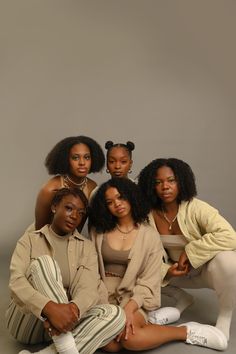 four young women posing for a photo in front of a gray background, with one sitting on the floor