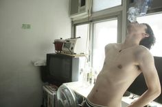 a shirtless man standing in front of a window with an air conditioner on his head