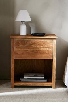 a wooden night stand next to a bed with a white lamp on top of it