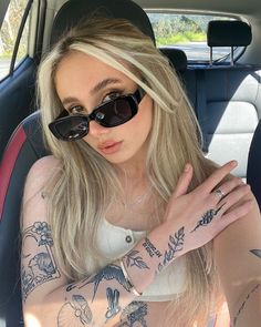 a woman sitting in the back seat of a car with tattoos on her arm and wrist