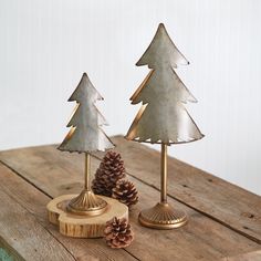 two metal christmas trees sitting on top of a wooden table next to a pine cone