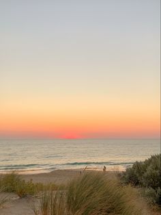 the sun is setting over the ocean and people are walking on the beach in the sand