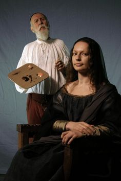 a woman sitting in a chair next to a man with a painting on his face