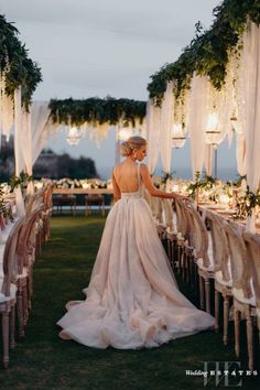 a woman in a wedding dress standing at the end of a long table with chairs