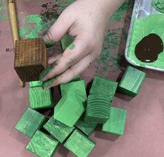 a child is painting with green paint on wood blocks