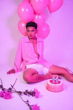 a man sitting in front of a cake with pink balloons on it and a birthday candle