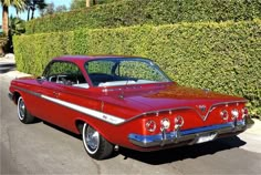 an old red car is parked on the side of the road next to a hedge