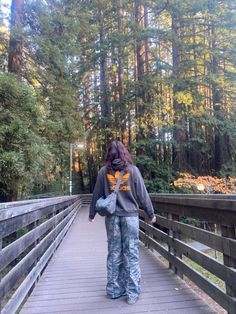 a woman walking across a wooden bridge in the woods