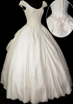 a white wedding dress with lace on the shoulders and neckline, is displayed in front of a black background