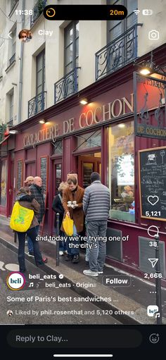 people are standing outside of a restaurant on the side of the street with their cell phones