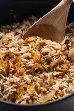 a wooden spoon is stirring rice and beans in a black pot with a wood spoon