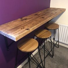 three stools are sitting in front of a wooden bar top on a purple wall