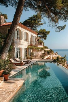 an outdoor swimming pool with lounge chairs and trees near the water in front of a large house