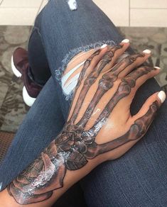 a woman's hand with skeleton hands and flowers on her left arm, while she is wearing blue jeans