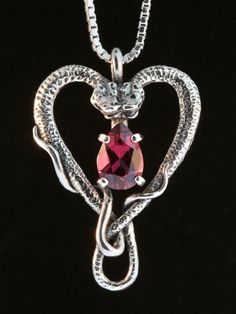 "Cast in solid sterling silver, two snakes entwine to form a Heart. A brilliant 9mm x 6mm gemstone is set in the center of the entwining snakes. Gift yourself or your special someone this unique Valentine as a pledge of your love. Dimensions are 1 1/4\" high and 7/8\" across. Please select your desired gemstone in the dropdown options menu. You may choose between a Blue Topaz, Citrine, Amethyst, Peridot, Mozambique Garnet or Black Onyx, or for an additional price, a Rhodolite Garnet. Although we Snake Chain Jewelry For Valentine's Day Anniversary, Sterling Silver Snake Jewelry For Anniversary, Elegant Sterling Silver Snake Jewelry, Snake Heart, Cast Jewelry, Two Snakes, Serpent Necklace, Magic Store, Necklace Snake