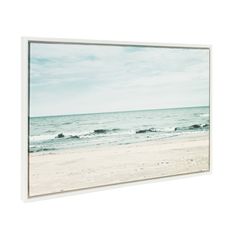 an empty beach with waves coming in to the shore and blue sky above, framed print on canvas