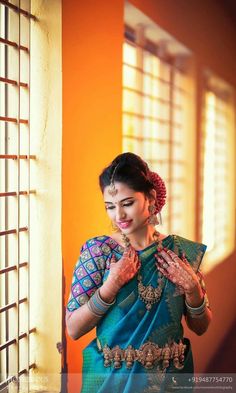 a woman in a blue and green sari standing by a window with sunlight coming through the windows