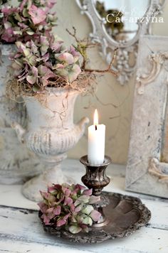 a candle is sitting on a plate next to some flowers and an ornate mirror in the background