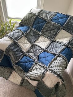 a blue and gray blanket sitting on top of a bed next to a plant in a window sill