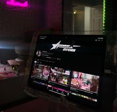 a laptop computer sitting on top of a table in front of a pink neon light