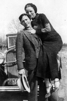 an old black and white photo of two people standing next to each other in front of a car