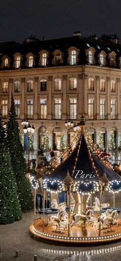 a merry go round in front of a large building with christmas trees and lights on it