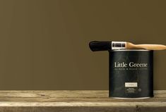 a paint can with a brush in it sitting on a wooden table next to a brown wall