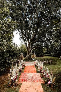 an outdoor ceremony area with flowers and rugs on the ground, trees in the background