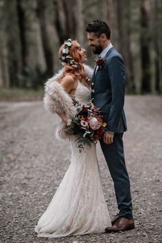 a bride and groom standing in the middle of a dirt road with trees behind them