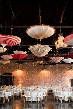 many umbrellas are hanging from the ceiling in a room with tables, chairs and chandeliers