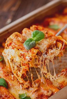 a piece of lasagna being lifted from a casserole dish with basil