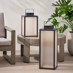 three lanterns sitting on top of a wooden table next to a chair and potted plant