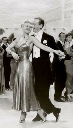 a man and woman dance together in front of a group of people wearing formal clothes