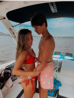 two people in swimsuits standing on a boat looking at each other and smiling